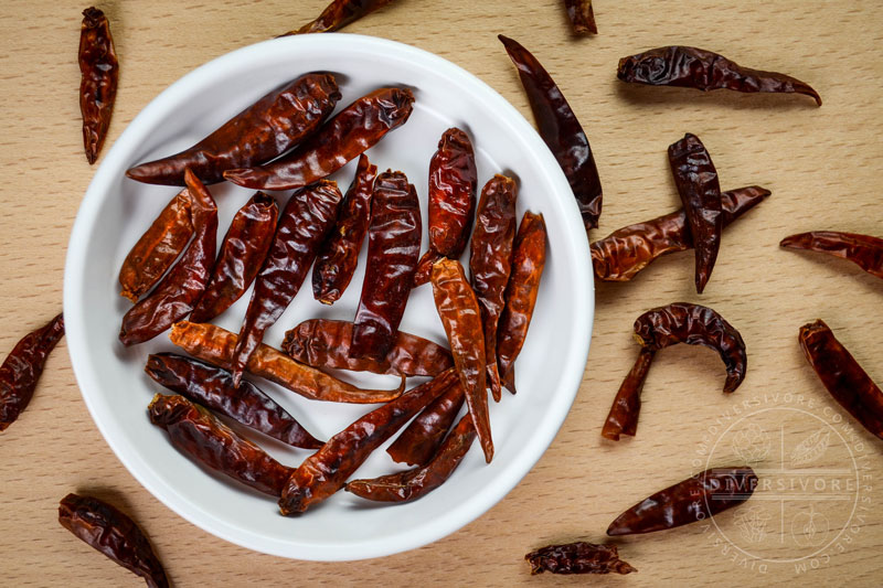 Loose Chinese chilies (aka chiles Japones) in a white bowl and on a table top