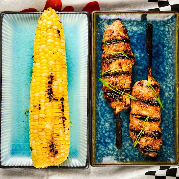Grilled chicken tsukune and grilled miso-butter corn on two blue plates