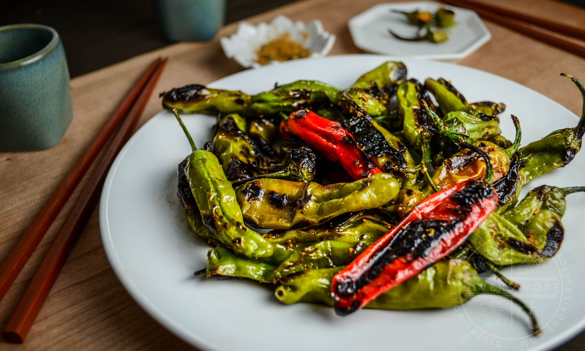 Charred shishito peppers with a sweet and spicy shichimi togarashi glaze on a white plate