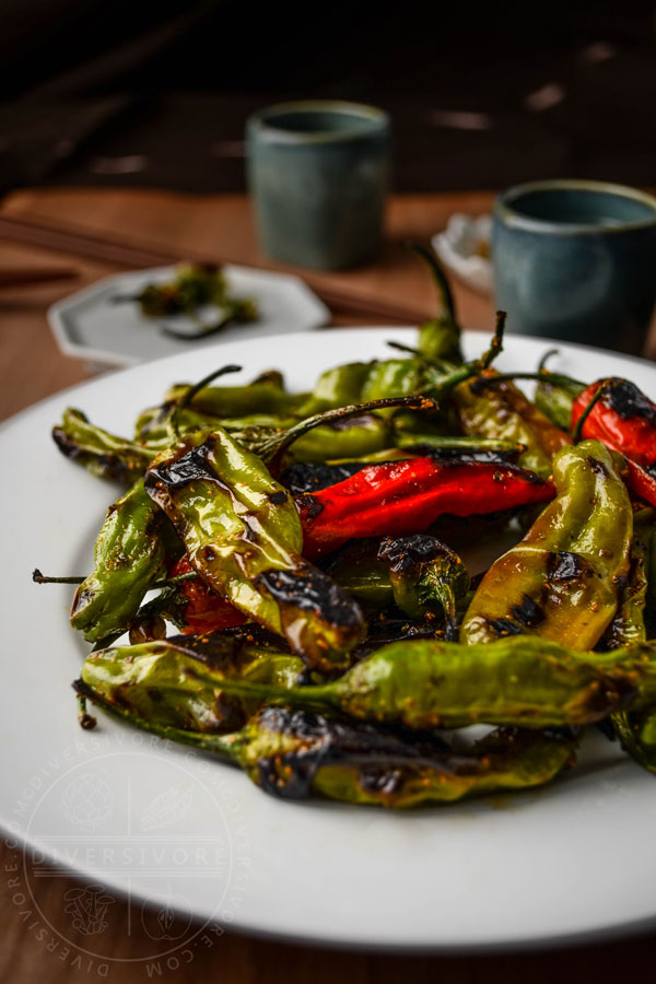 Charred shishito peppers with a sweet and spicy shichimi togarashi glaze on a white plate