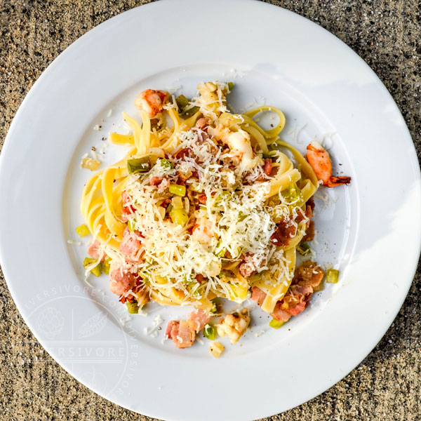 Fettuccine with green tomatoes, bacon, and prawns on a large white plate