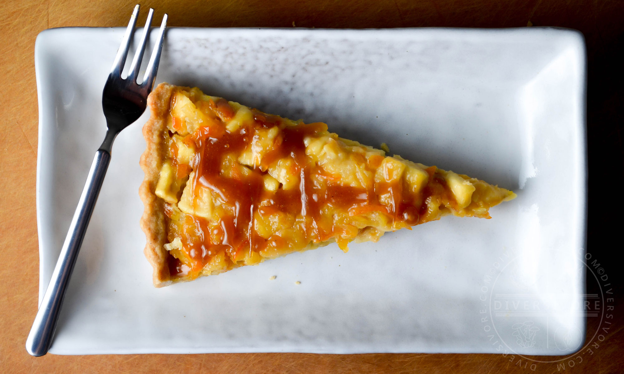 A slice of kumquat apple tart with whiskey caramel on a rectangular plate with a small dessert fork