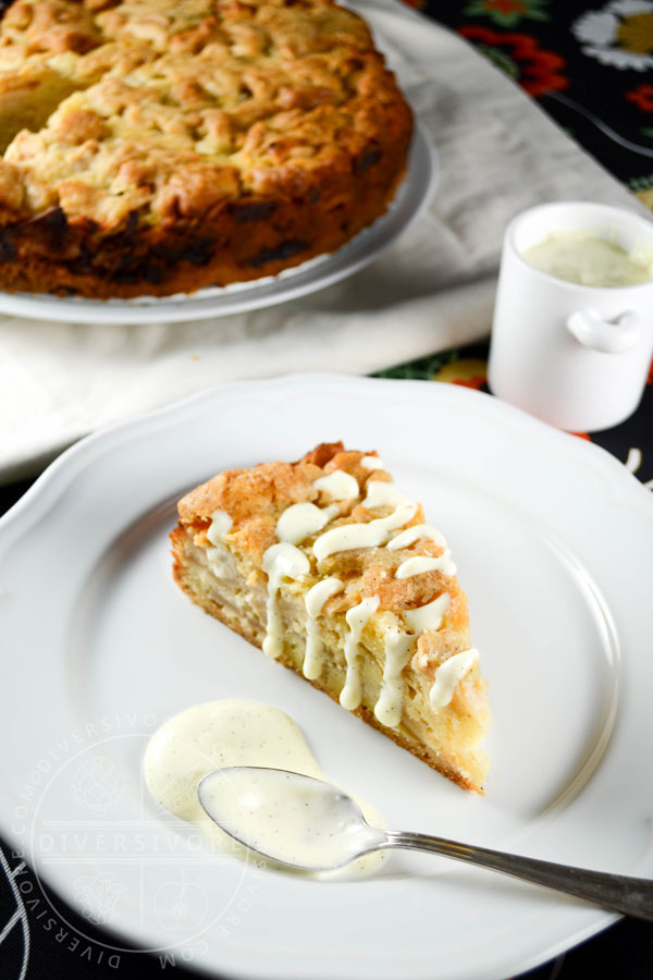 A slice of Swedish apple cake with vanilla sauce on a plate, in front of the rest of the cake