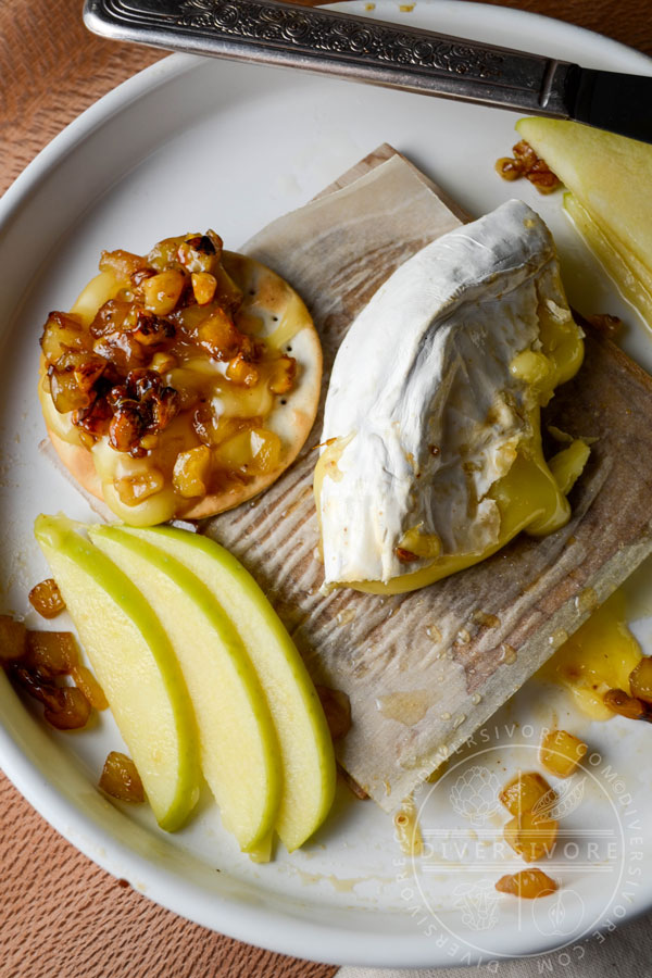 A leftover slice of baked brie alongside apple slices and a cracker topped with cheese and apple-walnut mixture.