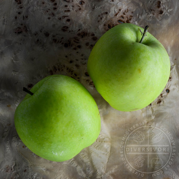 Two mutsu (crispin) apples on a burlwood background