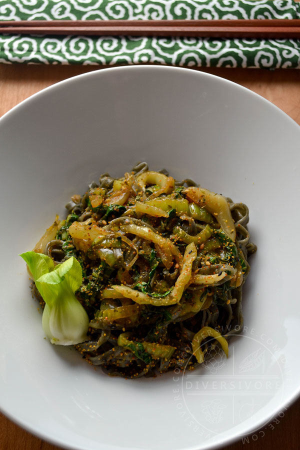 Garlic and lemon bok choy with black sesame noodles in a large white bowl, garnished with a fresh baby bok choy