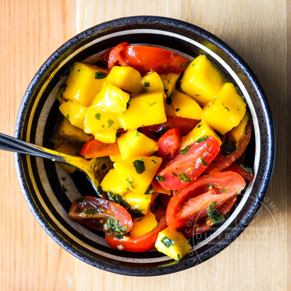 Mango and tomato salad with mint chimichurri in a patterned black bowl with a serving spoon