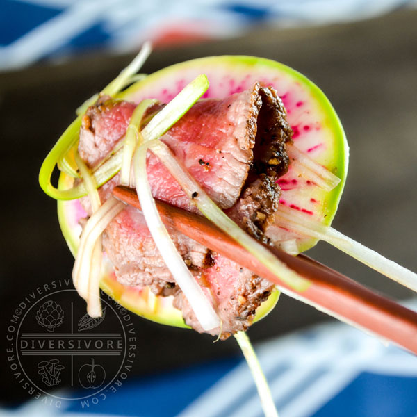 Slices of beef tataki, served with watermelon radish, held by a pair of chopsticks