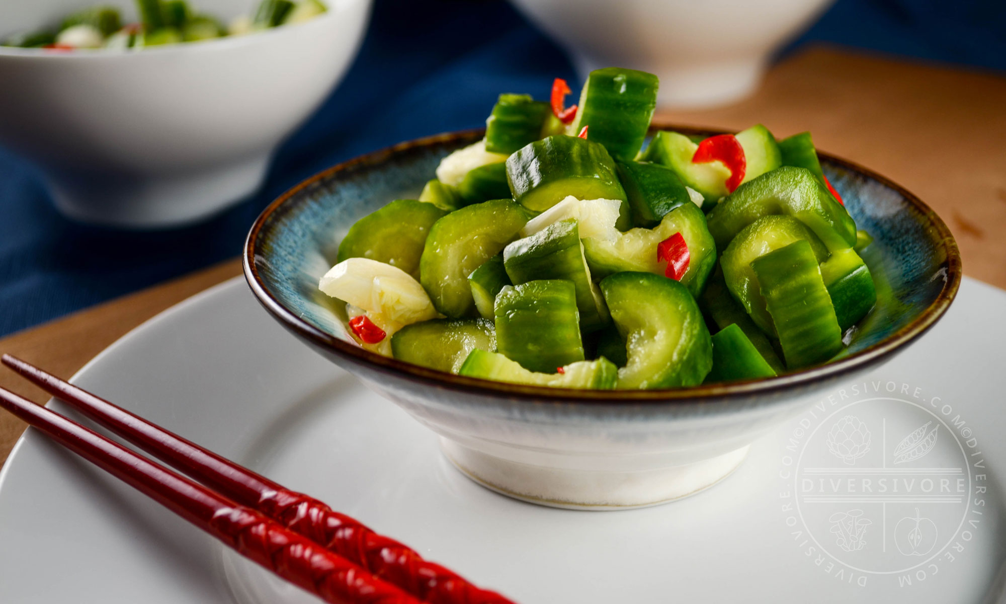 Chinese garlic cucumbers (Liangban Huanggua) in a small ceramic bowl, on a plate with red chopsticks