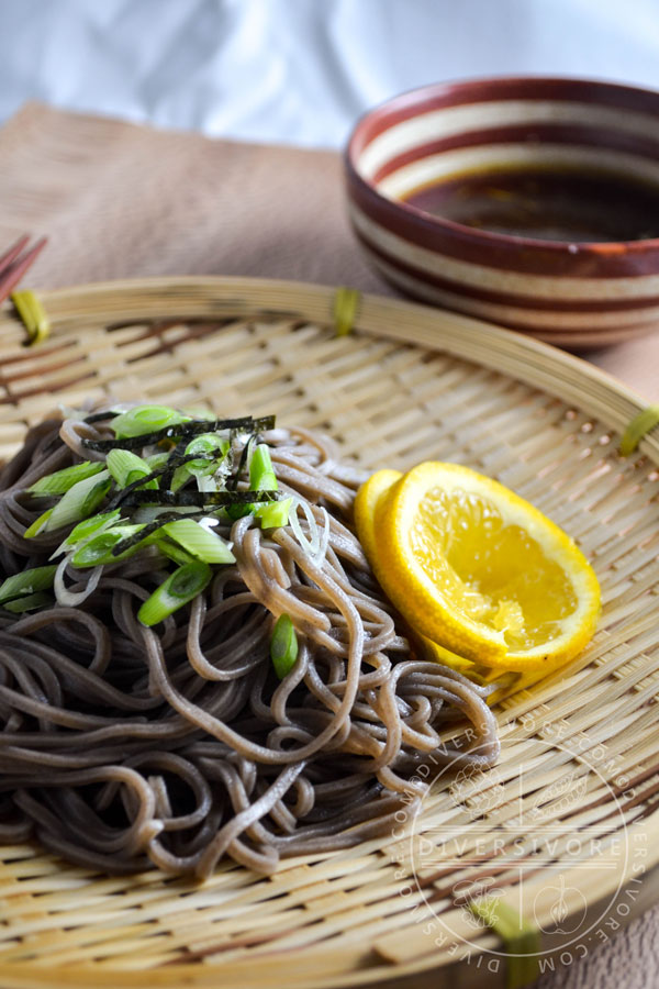 Mandelo Zaru Soba on a Japanese zaru (draining basket), topped with nori and scallions, and served with tsuyu (dipping sauce).