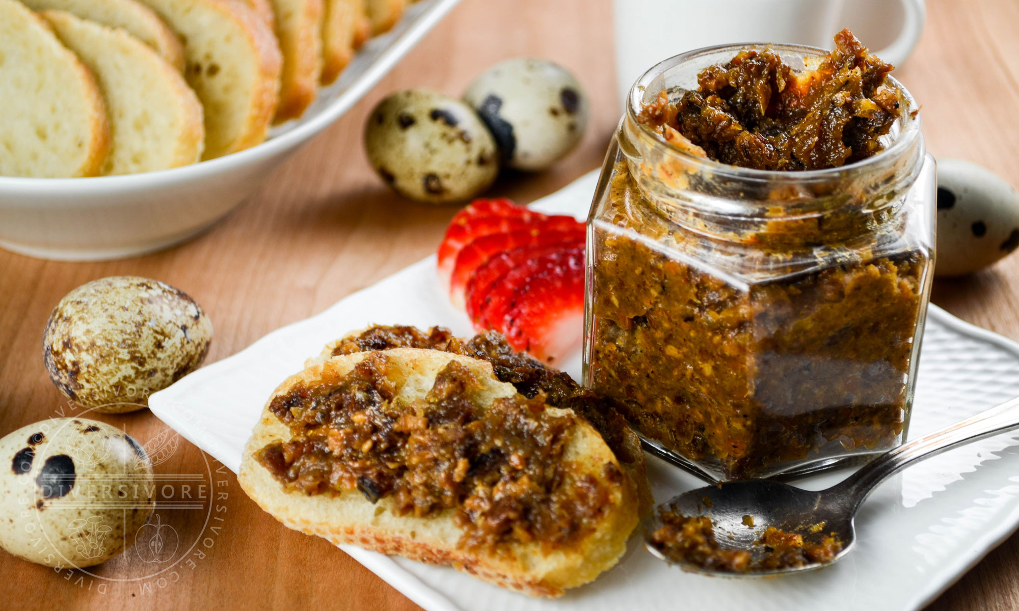 Bacon marmalade in a hexagonal glass jar with a spoon, bread, strawberries, and scattered quail eggs