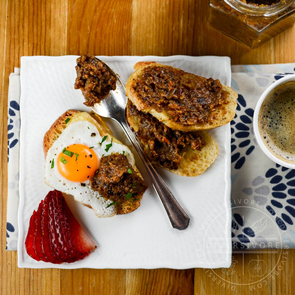 Bacon marmalade in a hexagonal glass jar with a spoon, bread, strawberries, and scattered quail eggs