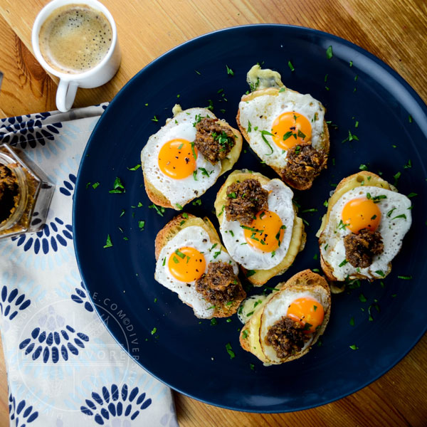 Croque petite sandwiches made with rounds of baguette, fried quail eggs, and bacon marmalade, served on a dark blue plate