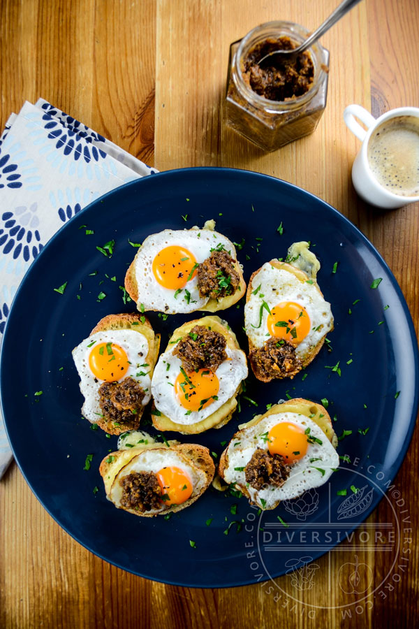 Croque petite sandwiches made with rounds of baguette, fried quail eggs, and bacon marmalade, served on a dark blue plate