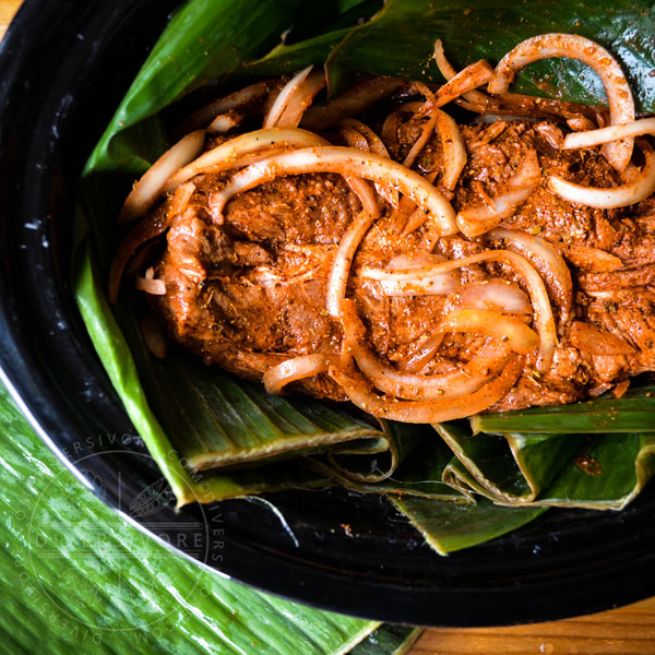 Uncooked puerco pibil with achiote and onions, wrapped in banana leaves to prepare it for cooking