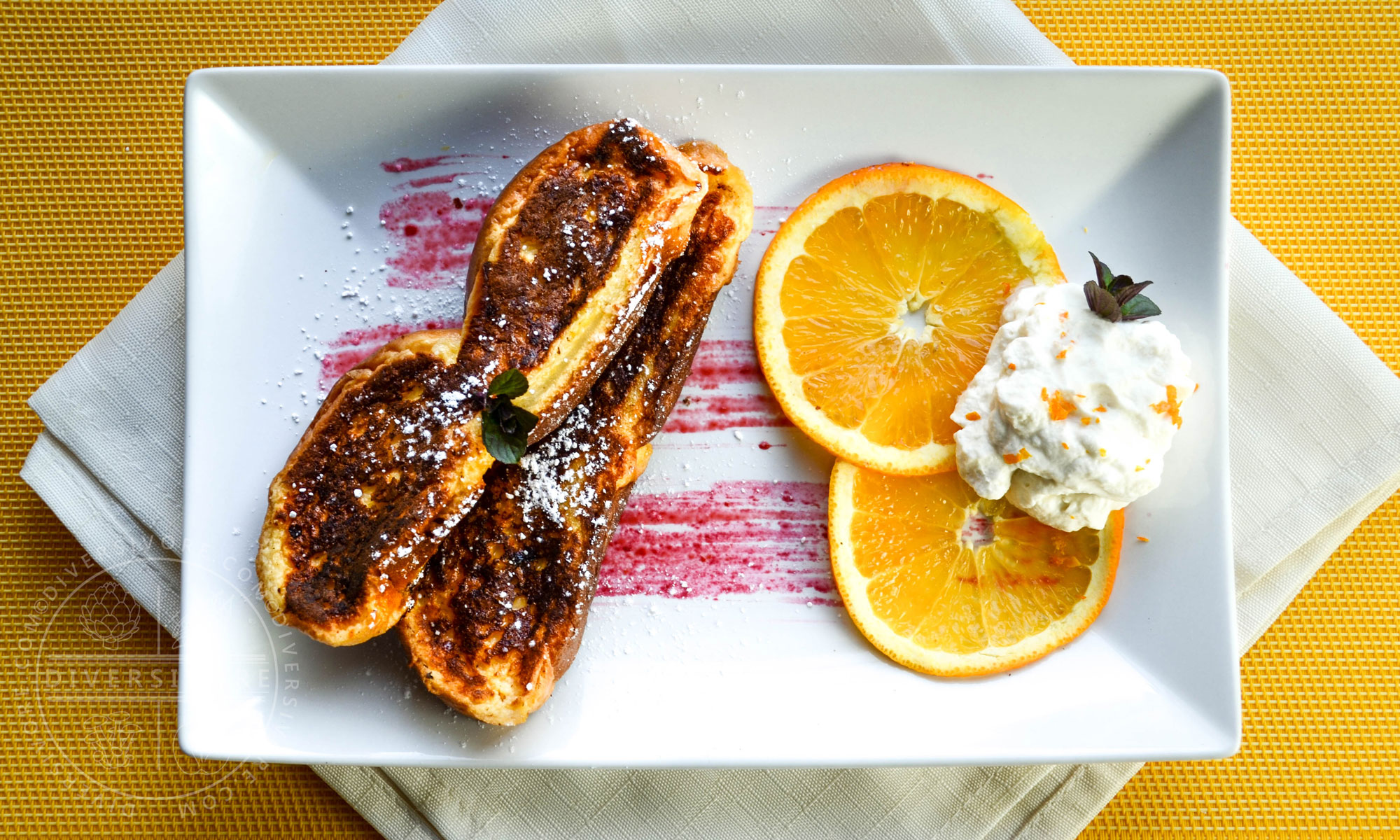 Seville Orange French Toast on a rectangular white plate with orange slices and maple whipped cream