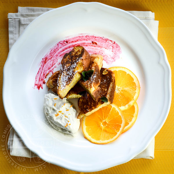 Seville orange french toast with maple whipped cream and orange slices on a white plate