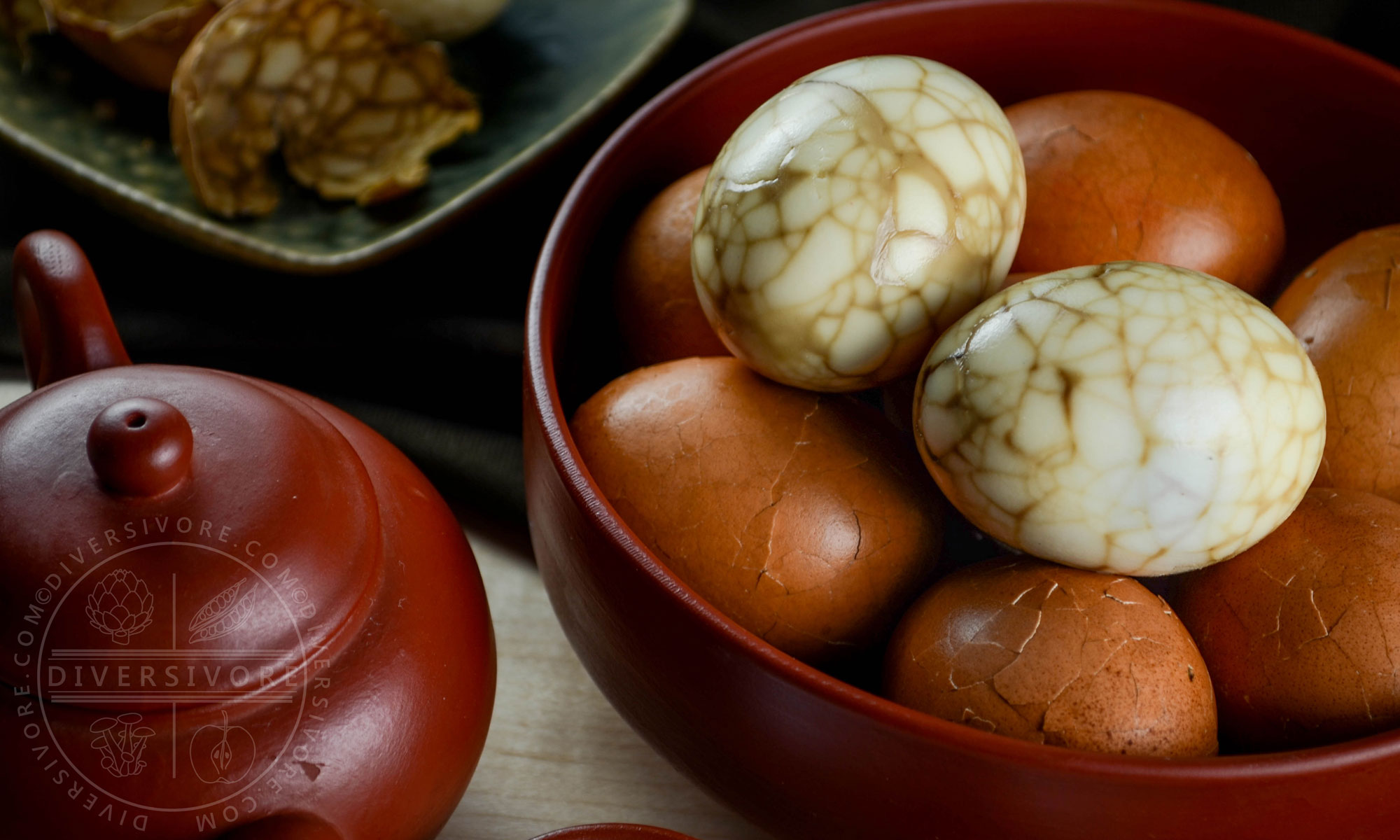 Taiwanese tea eggs, both peeled and unpeeled, in a bowl beside a clay tea pot