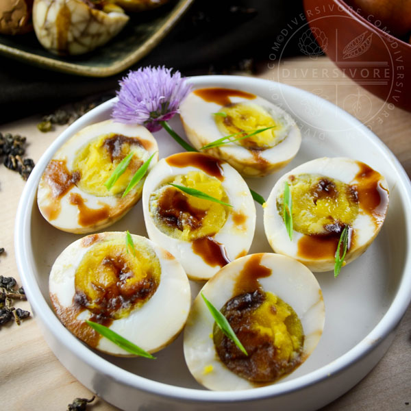 Halved Taiwanese tea eggs in a bowl with sauce and chives