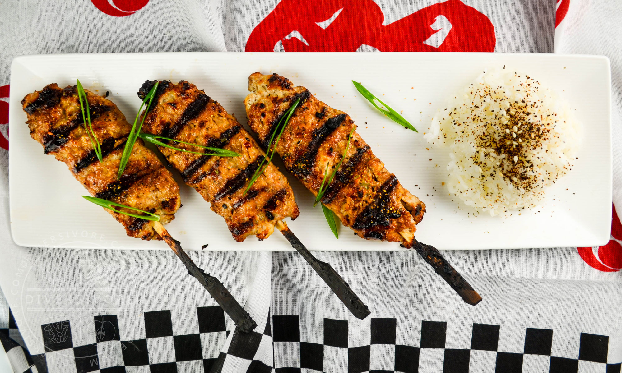 Grilled chicken tsukune (meatballs) on bamboo skewers, served with green onions and rice topped with seaweed and sesame seeds