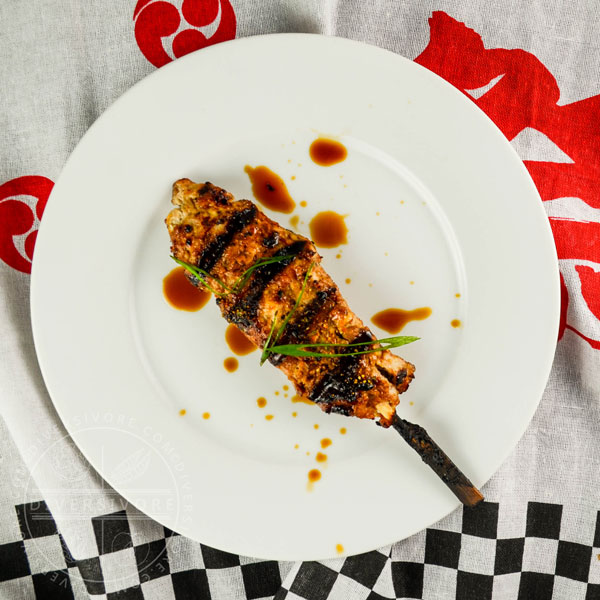 Chicken tsukune (meatball) on a skewer with homemade sauce on a white plate