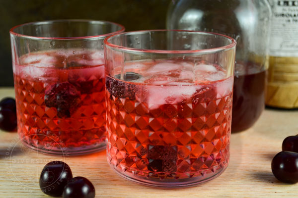 Clock Calm - a Red Currant Gin & Tonic Cocktail - in a decorative tumbler, surrounded by sour cherries