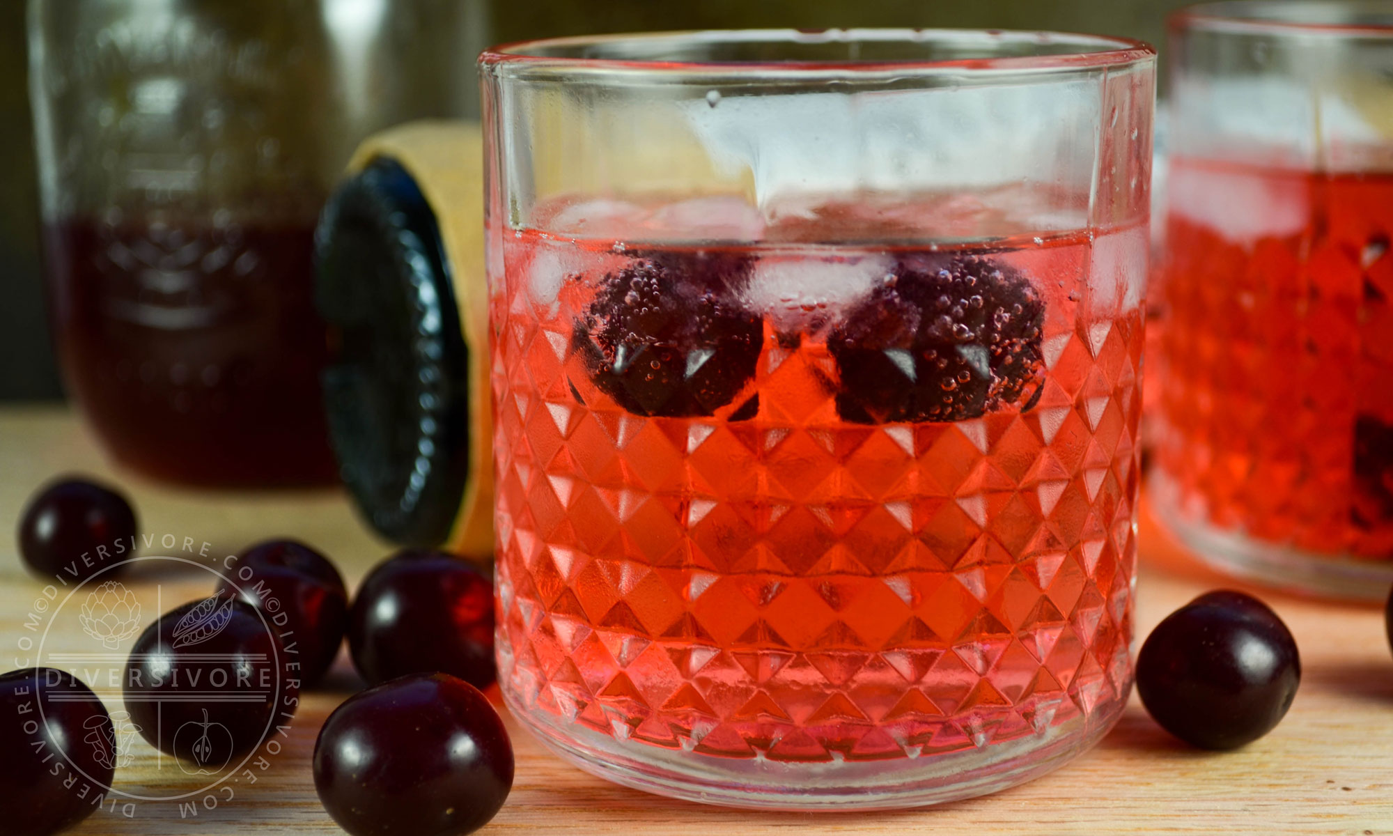 Clock Calm - a Red Currant Gin & Tonic Cocktail - in a decorative tumbler, surrounded by sour cherries