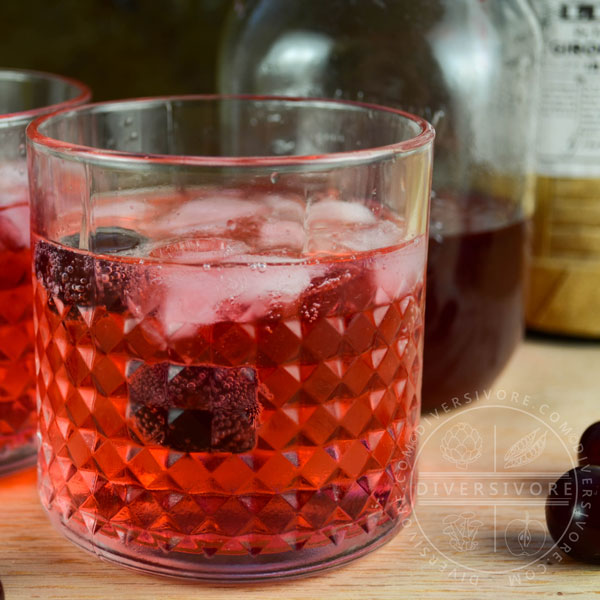 Clock Calm - a Red Currant Gin & Tonic Cocktail - in a decorative tumbler, surrounded by sour cherries