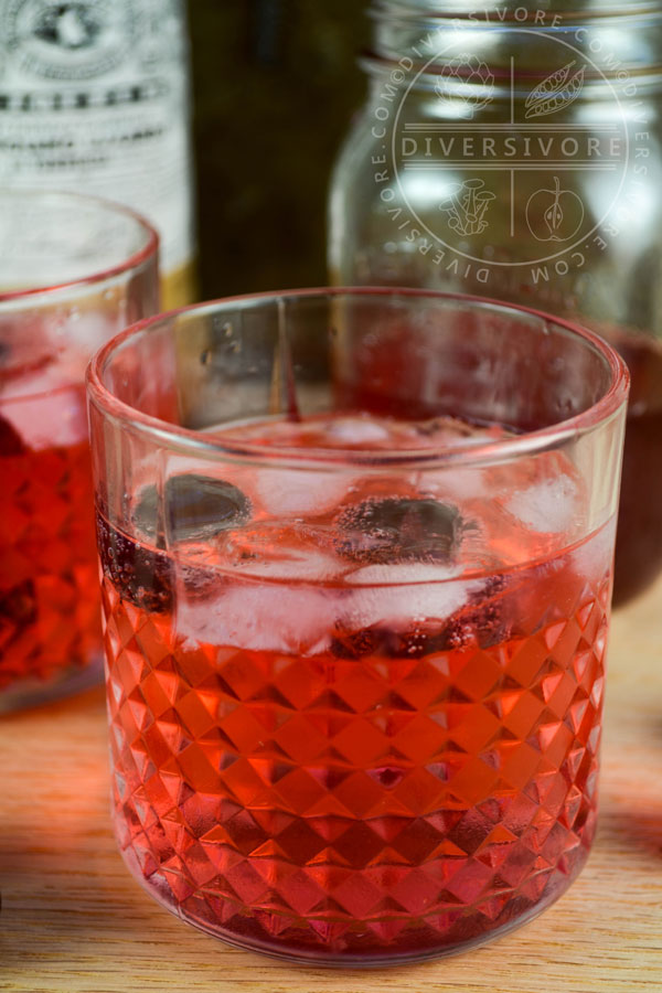 Clock Calm - a Red Currant Gin & Tonic Cocktail - in two decorative tumbler, surrounded by sour cherries