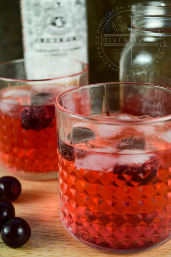 Clock Calm - a Red Currant Gin & Tonic Cocktail - in two decorative tumblers, surrounded by sour cherries