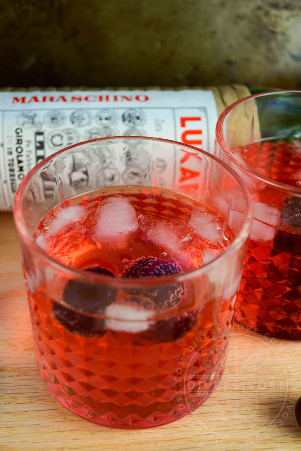 Clock Calm - a Red Currant Gin & Tonic Cocktail - in two decorative tumblers, in front of a bottle of Luxardo Maraschino liqueur.