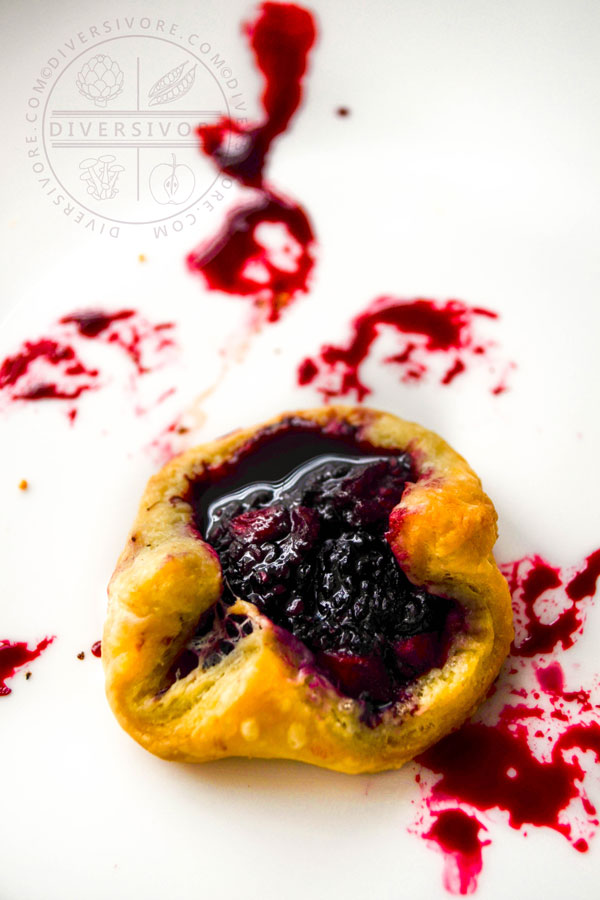 Dewberry and apple puff pastry tart on a white plate with blackberry juice splatters