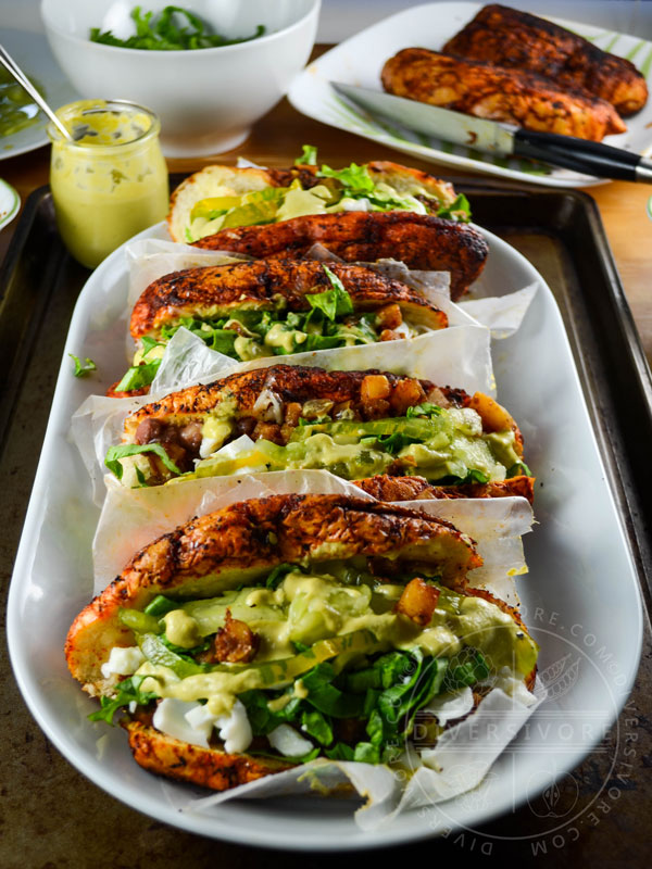 Four Pambazos con Huevos - Mexican bread soaked in guajillo chili sauce, fried, and filled with potatoes, spices, egg, and a creamy tomatillo sauce, served on a white platter