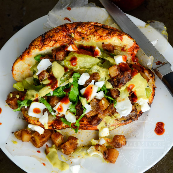 Pambazos con Huevos - Mexican bread soaked in guajillo chili sauce, fried, and filled with potatoes, spices, egg, and a creamy tomatillo sauce, served on a white plate with salsas