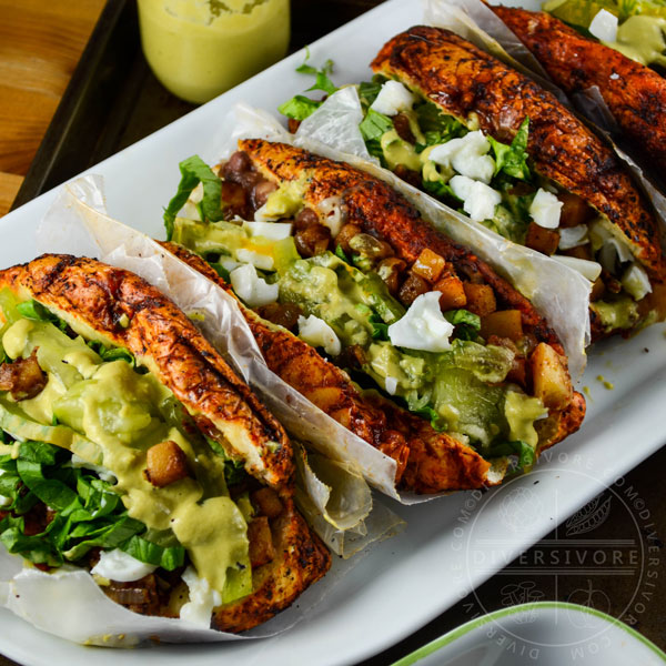 Four Pambazos con Huevos - Mexican bread soaked in guajillo chili sauce, fried, and filled with potatoes, spices, egg, and a creamy tomatillo sauce, served on a white platter