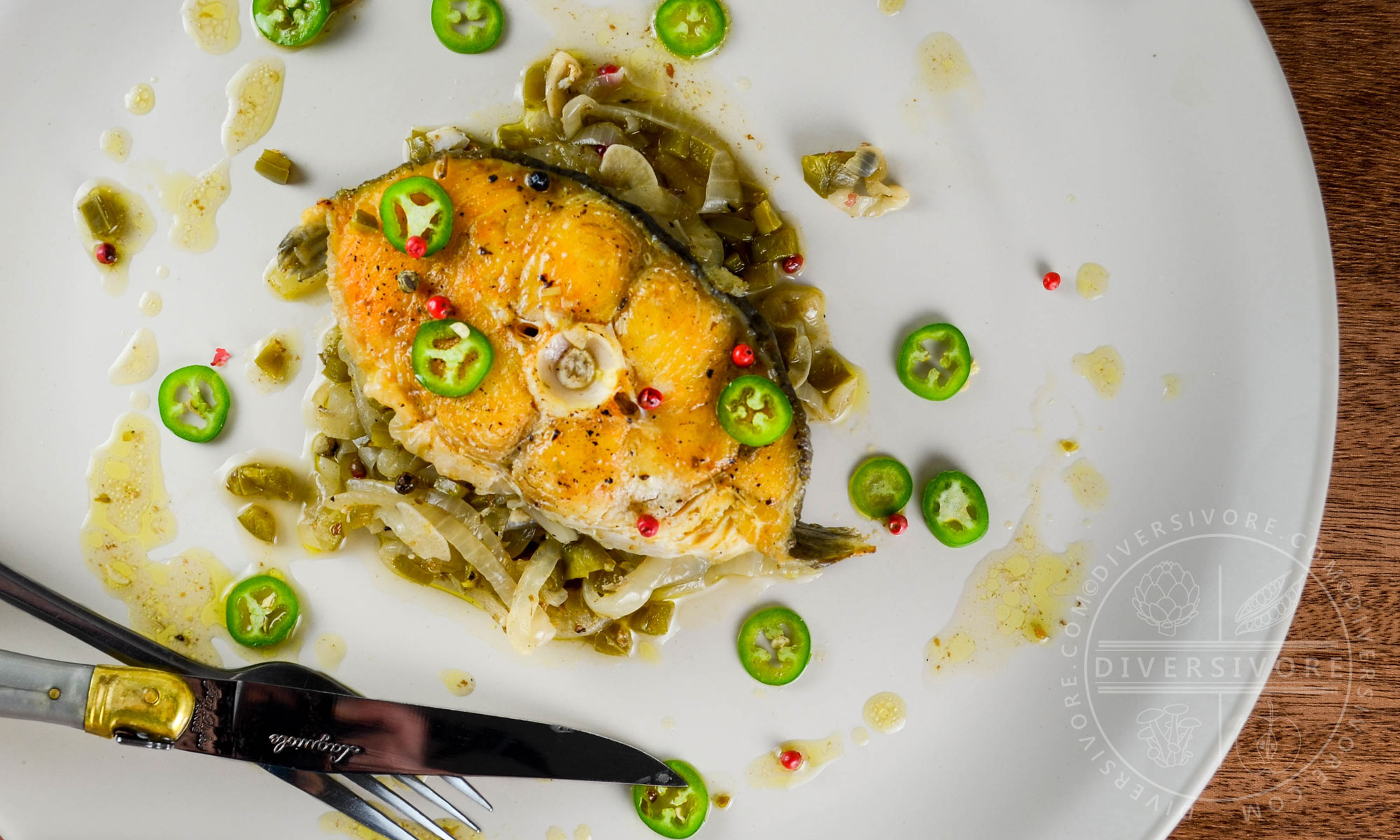 Halibut escabeche steaks with fresh jalapenos on a large beige plate with a fork and knife