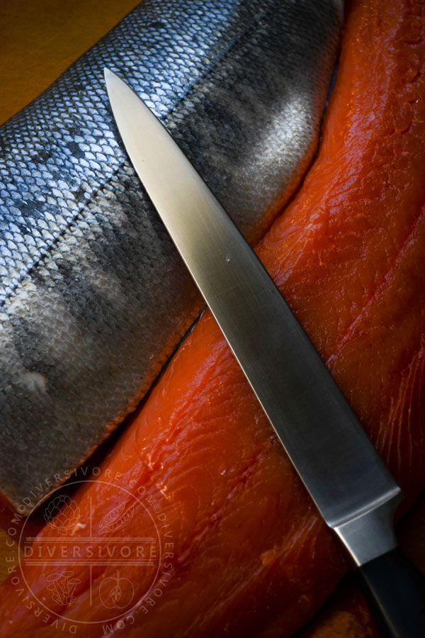 Keta salmon fillets, one skin-side up, one meat-side up, with a long slicing knife.