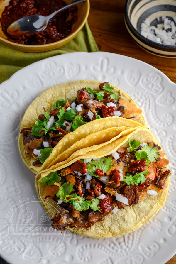 Pressure cooker Carnitas con Queso (tender beef bites with crispy melted cheese) served in corn tortillas on a textured white plate