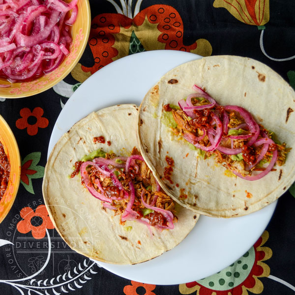 Pressure-cooked Puerco Pibil with pickled onions and guacamole, served in tortillas, flanked by smoky dried chili salsa