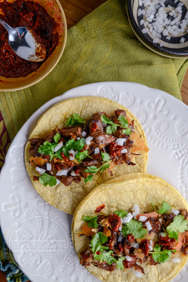 Carnitas con queso tacos on a textured white plate, topped with cilantro, onions, and k'uut bi ik salsa.