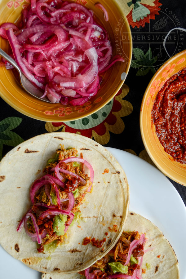 Pressure-cooked Puerco Pibil with pickled onions and guacamole, served in tortillas, flanked by smoky dried chili salsa