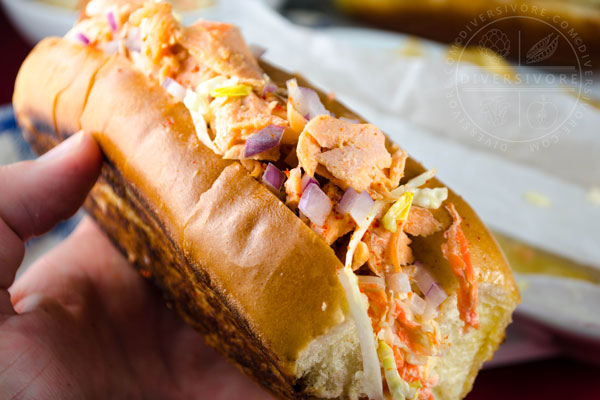 Salmon Guédille with coleslaw in a lobster roll bun and held in a hand