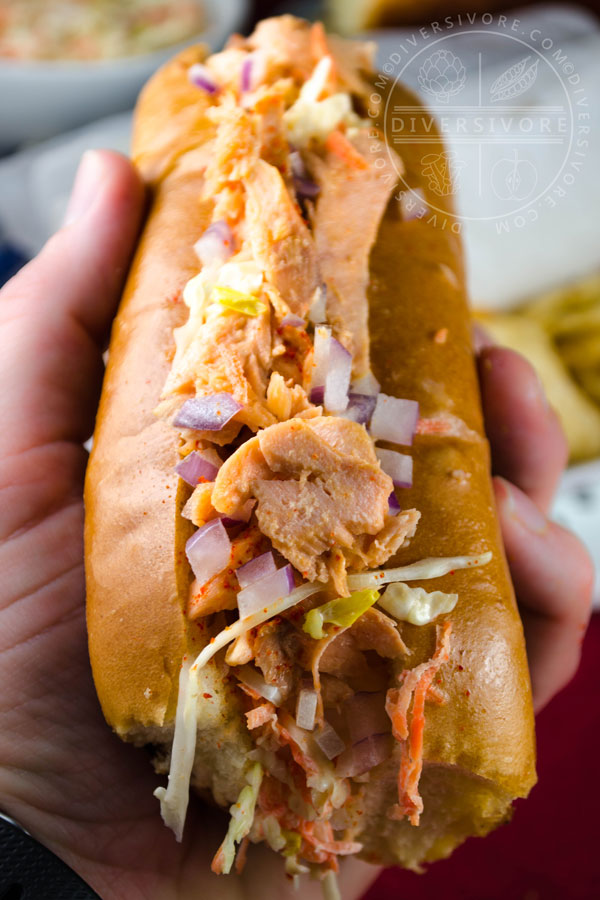 Salmon Guédille with coleslaw in a lobster roll bun and held in a hand
