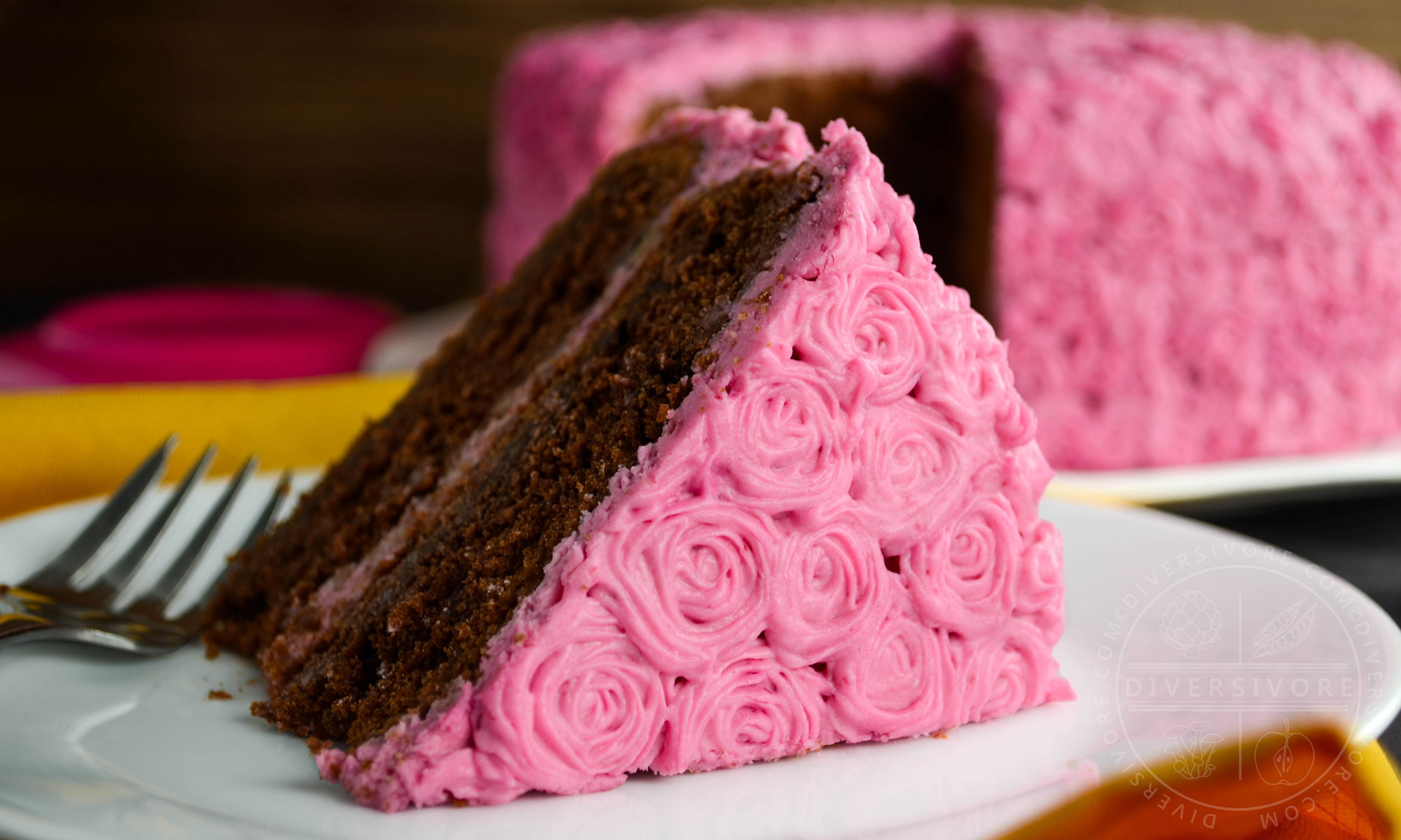 A slice of chocolate cake made with beetroot and candied pecans, frosted with pink cream cheese frosting rosettes
