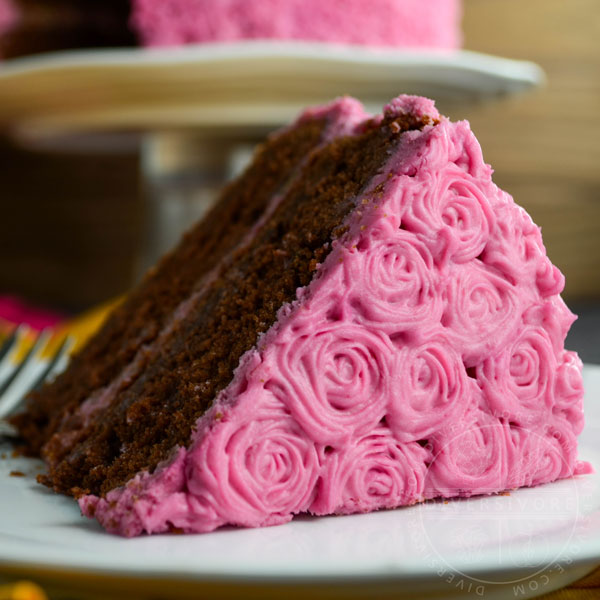 A slice of chocolate beet cake with pink cream cheese frosting on a white plate