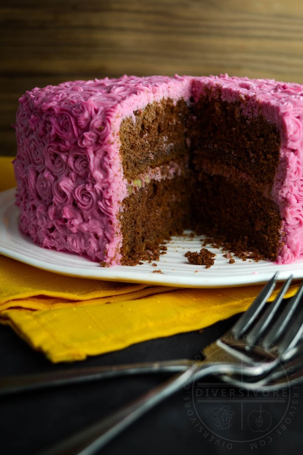 Chocolate cake made with beetroot and candied pecans, frosted with pink cream cheese frosting rosettes, shown on a platter with a slice removed