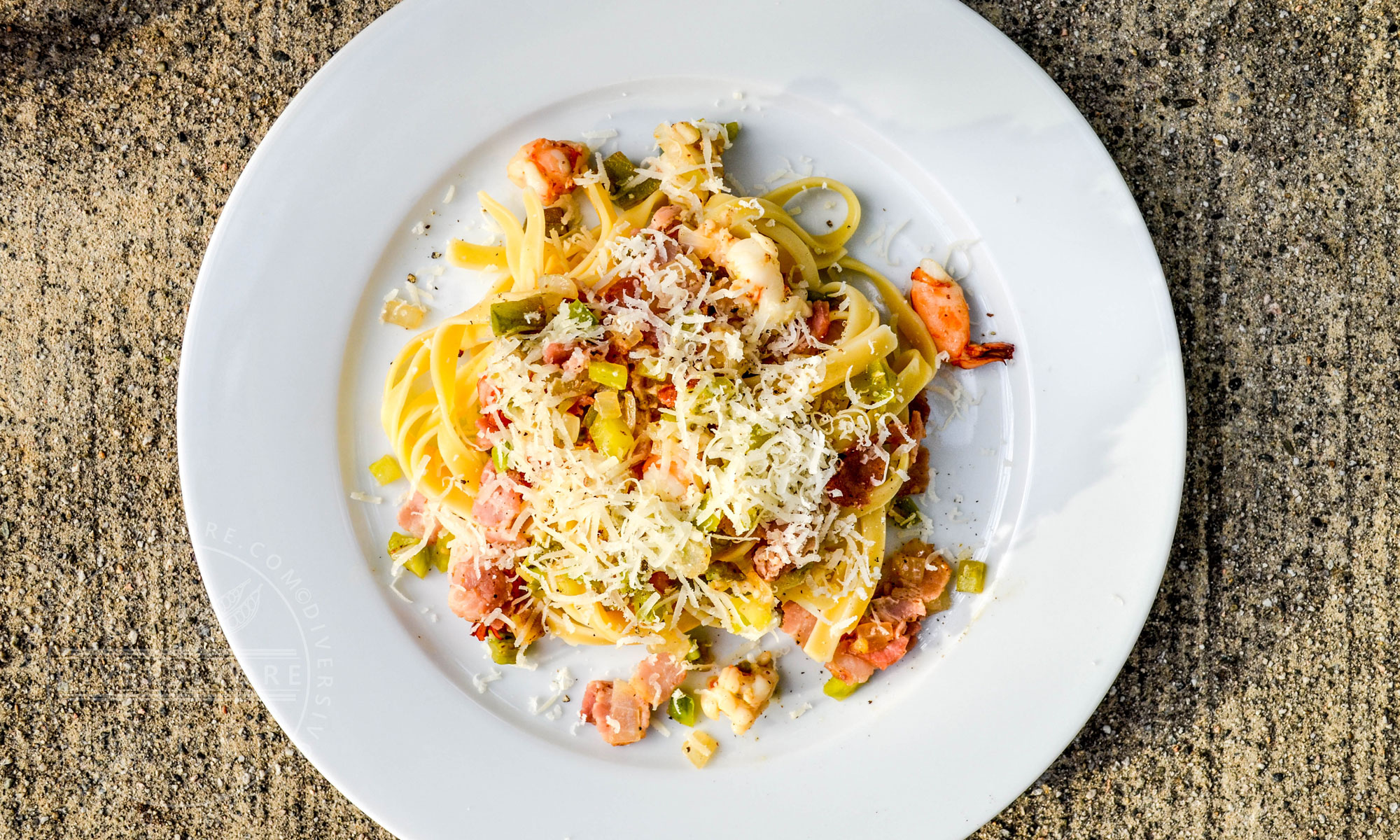 Fettuccine with green tomatoes, bacon, and prawns on a large white plate