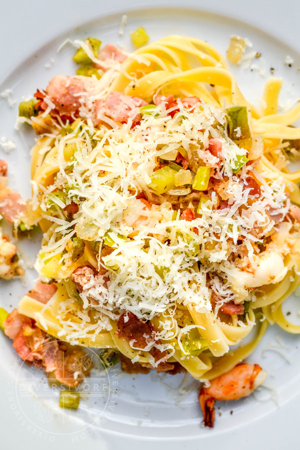 Fettuccine with green tomatoes, bacon, and prawns on a large white plate