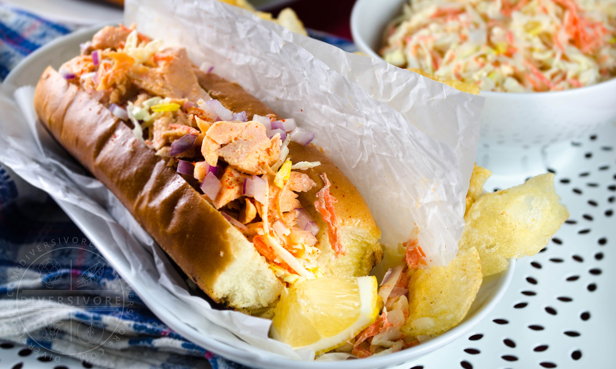 Salmon Guédille with coleslaw in a lobster roll bun, served with chips and a lemon wedge