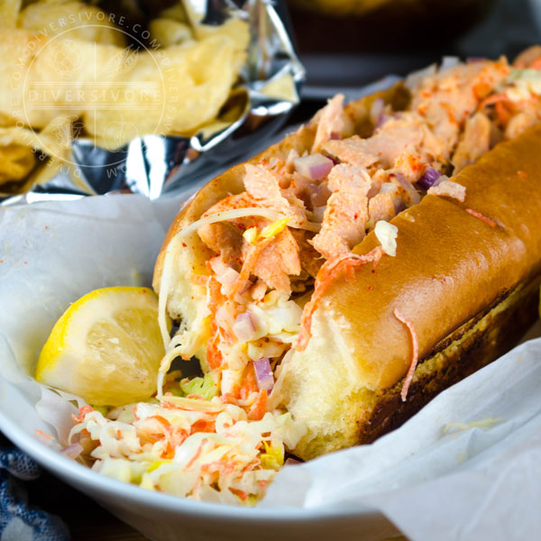 Salmon Guédille with coleslaw in a lobster roll bun, served with chips and a lemon wedge